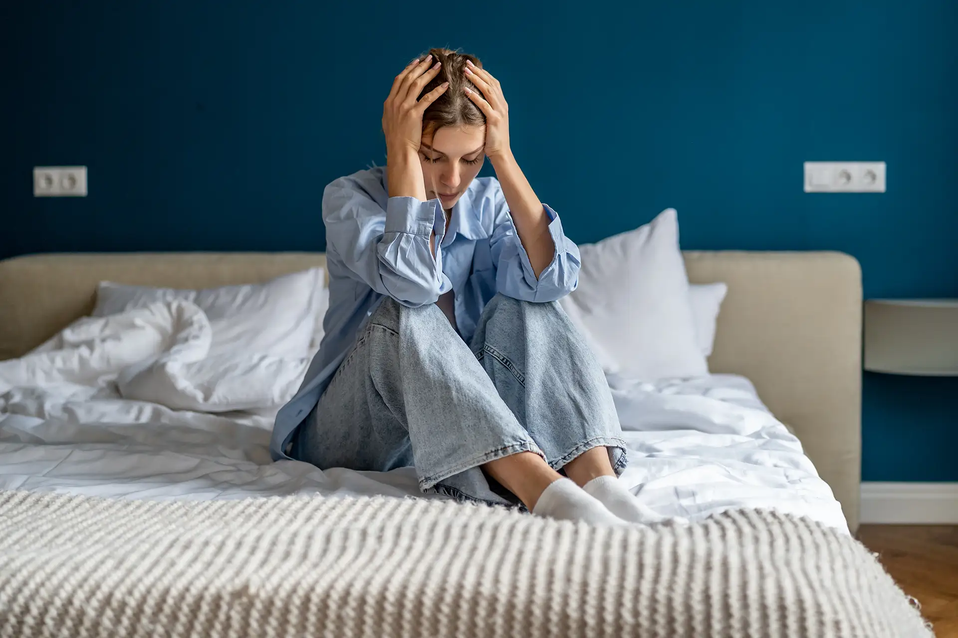 Frau sitzt auf ihrem Bett und fast sich an den Kopf.