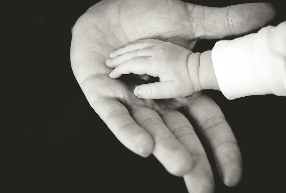 Urvertrauen - die Hand eines Babys in der Handfläche eines Mannes